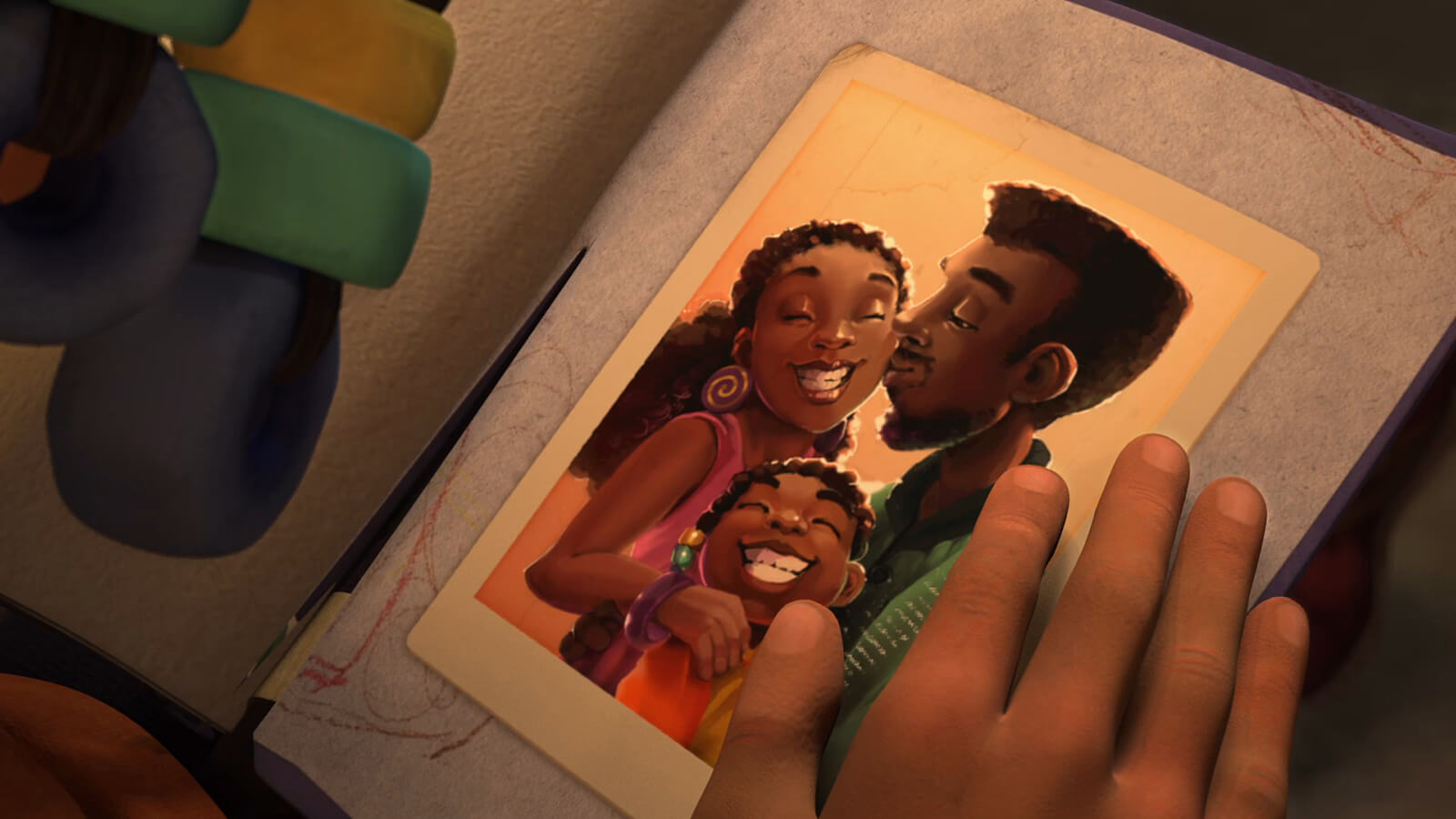 A hand is on a scrapbook containing a photo of a family, with a man kissing a smiling woman and a smiling girl below them