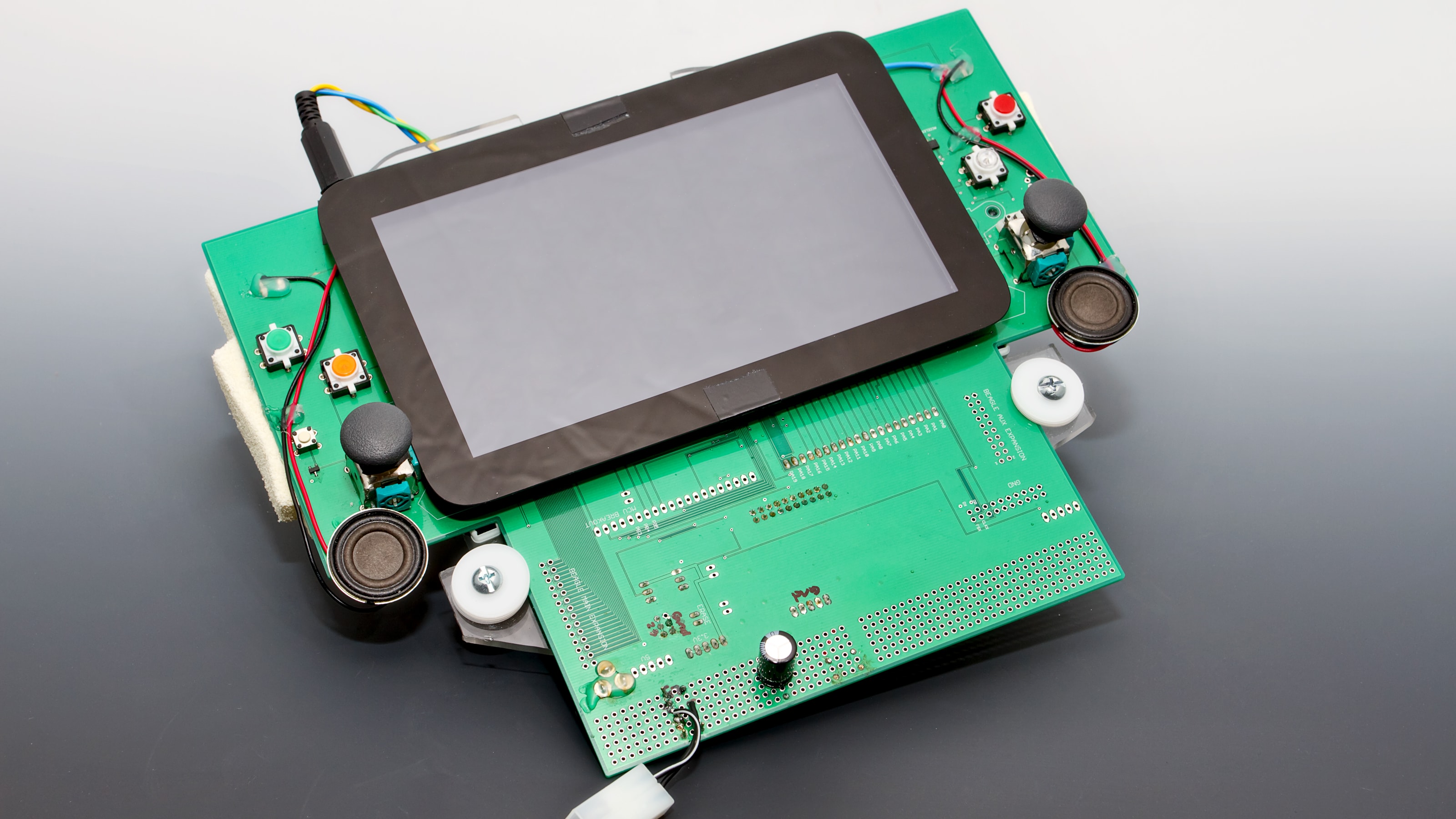 A screen mounted to a green circuit board with two control sticks.