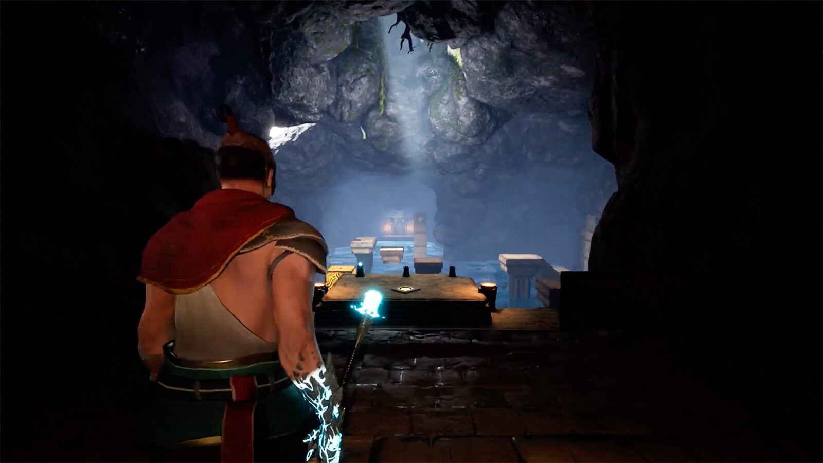 A man faces an opening in a cavern, holding a glowing spear.