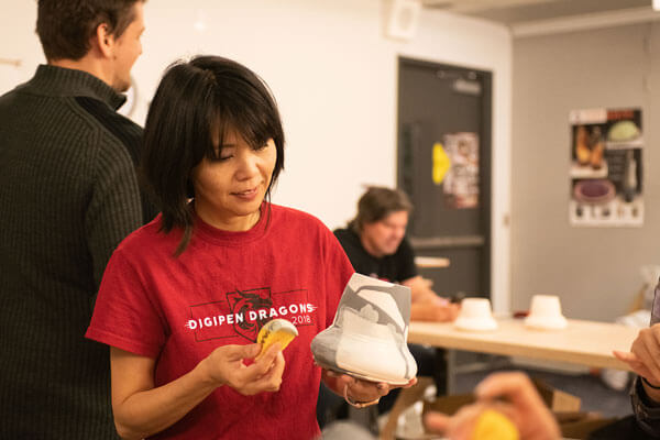 In an art studio, a woman in a red DigiPen Dragons t-shirt decorates a piece of kiln-fired pottery.