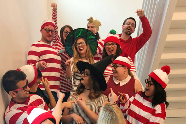 A handful of DigiPen staff wearing Waldo costumes pose in a white stariwell.