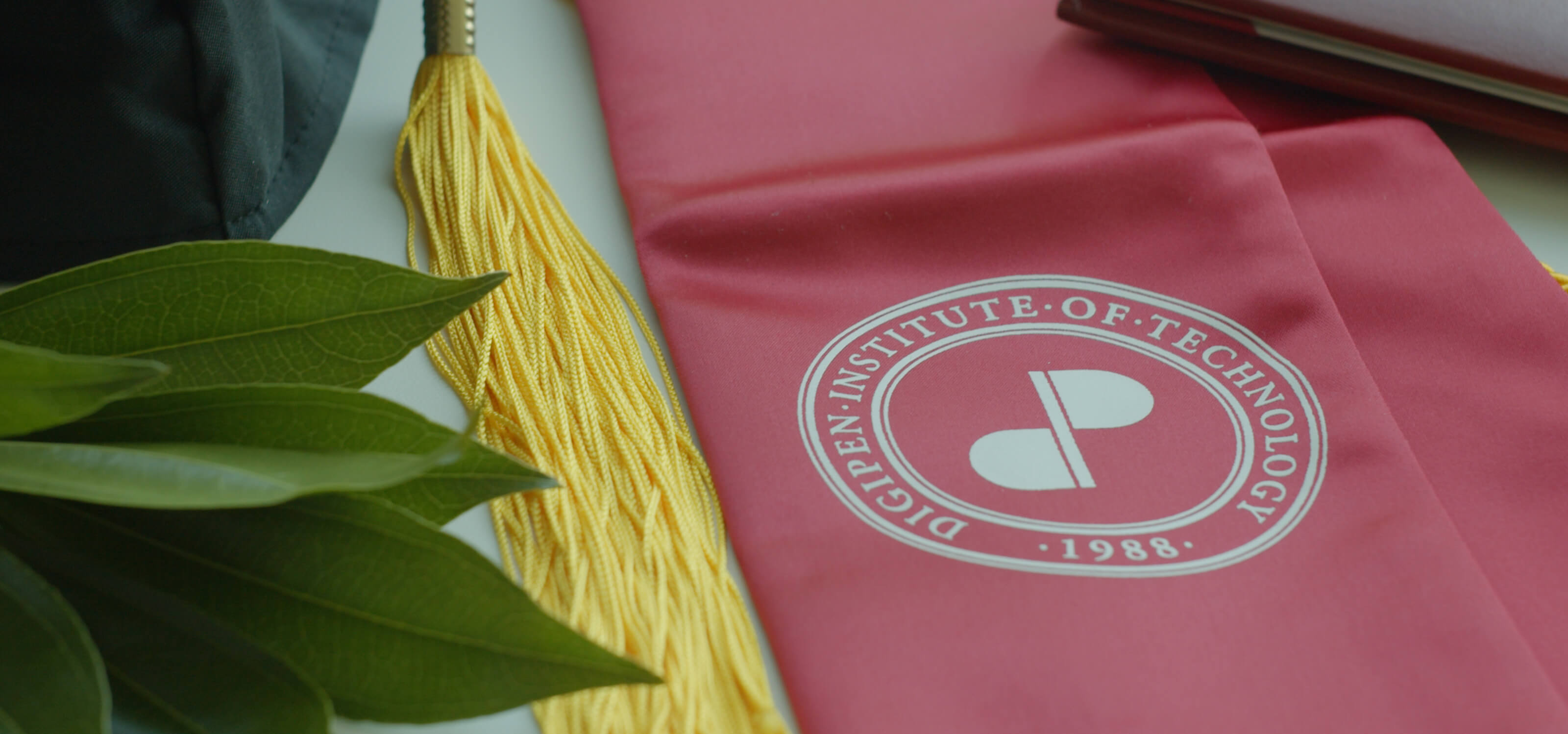 Red DigiPen graduation sash with a yellow tassel next to it