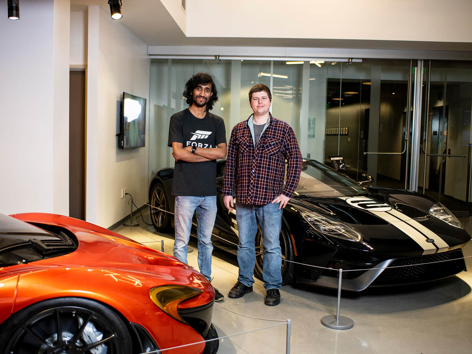 Michael Pitaniello and Deepak Chennakkadan stand next to luxury cars in the Turn 10 Studios lobby.