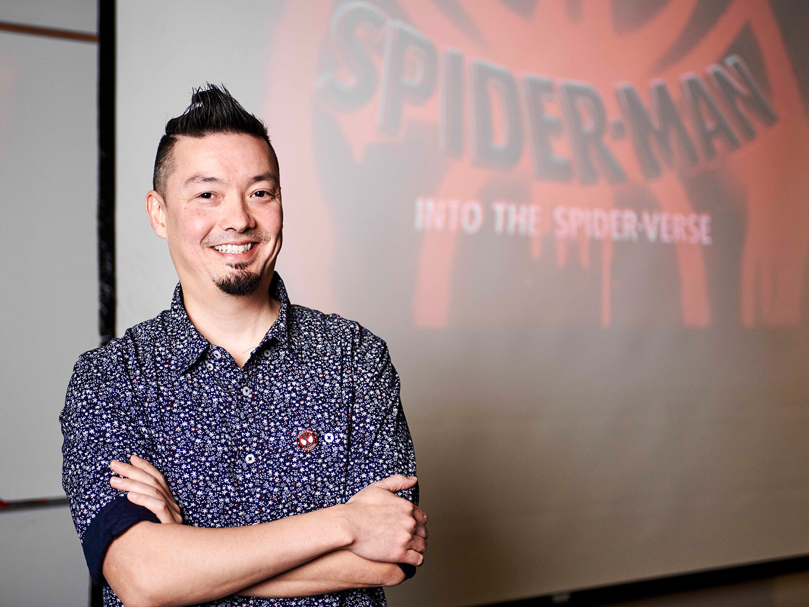 Nick Kondo smiles in front of a projection of Spider-Man: Into the Spider-Verse’s title card.