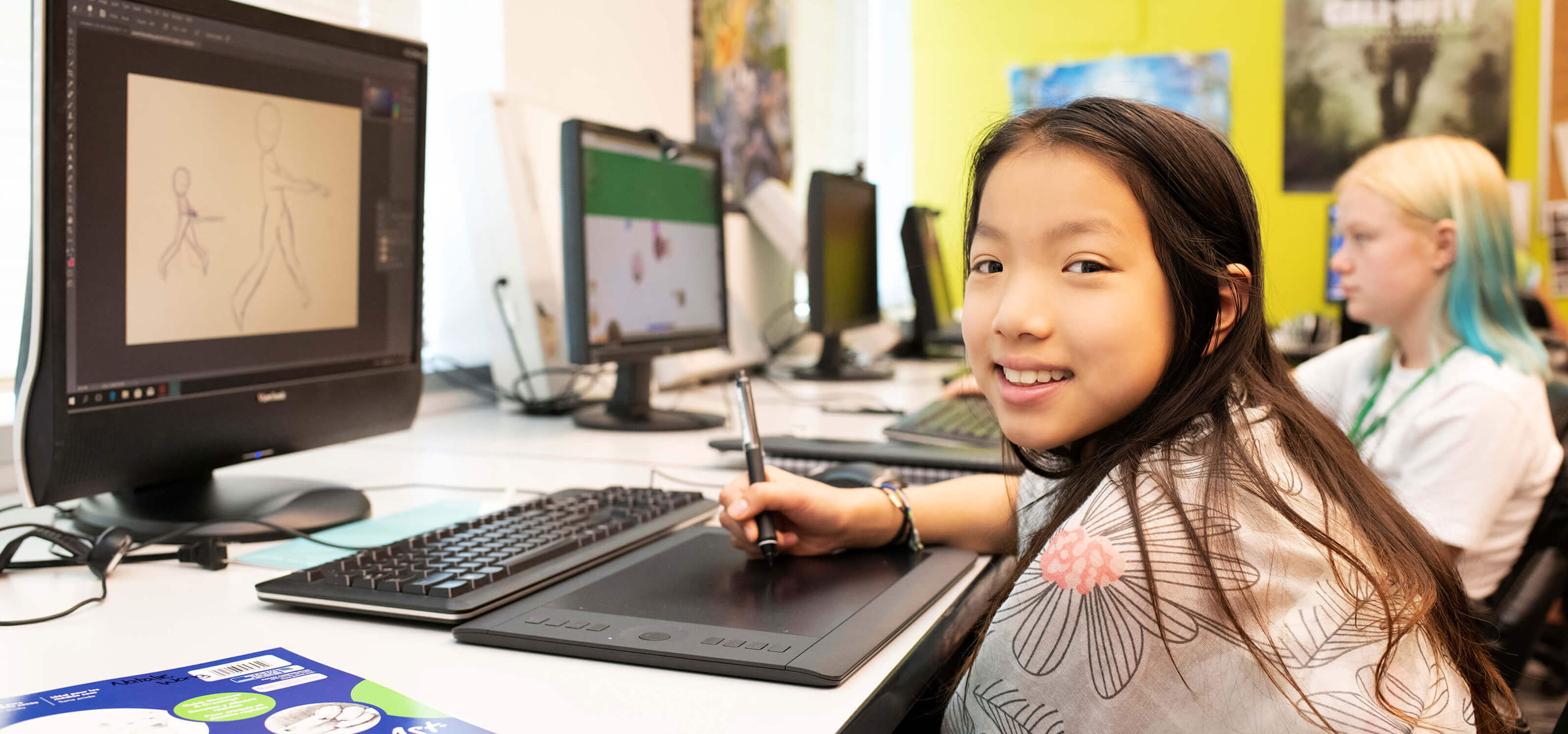 A young DigiPen Academy student smiling as she sits at a computer in a classroom at the DigiPen campus