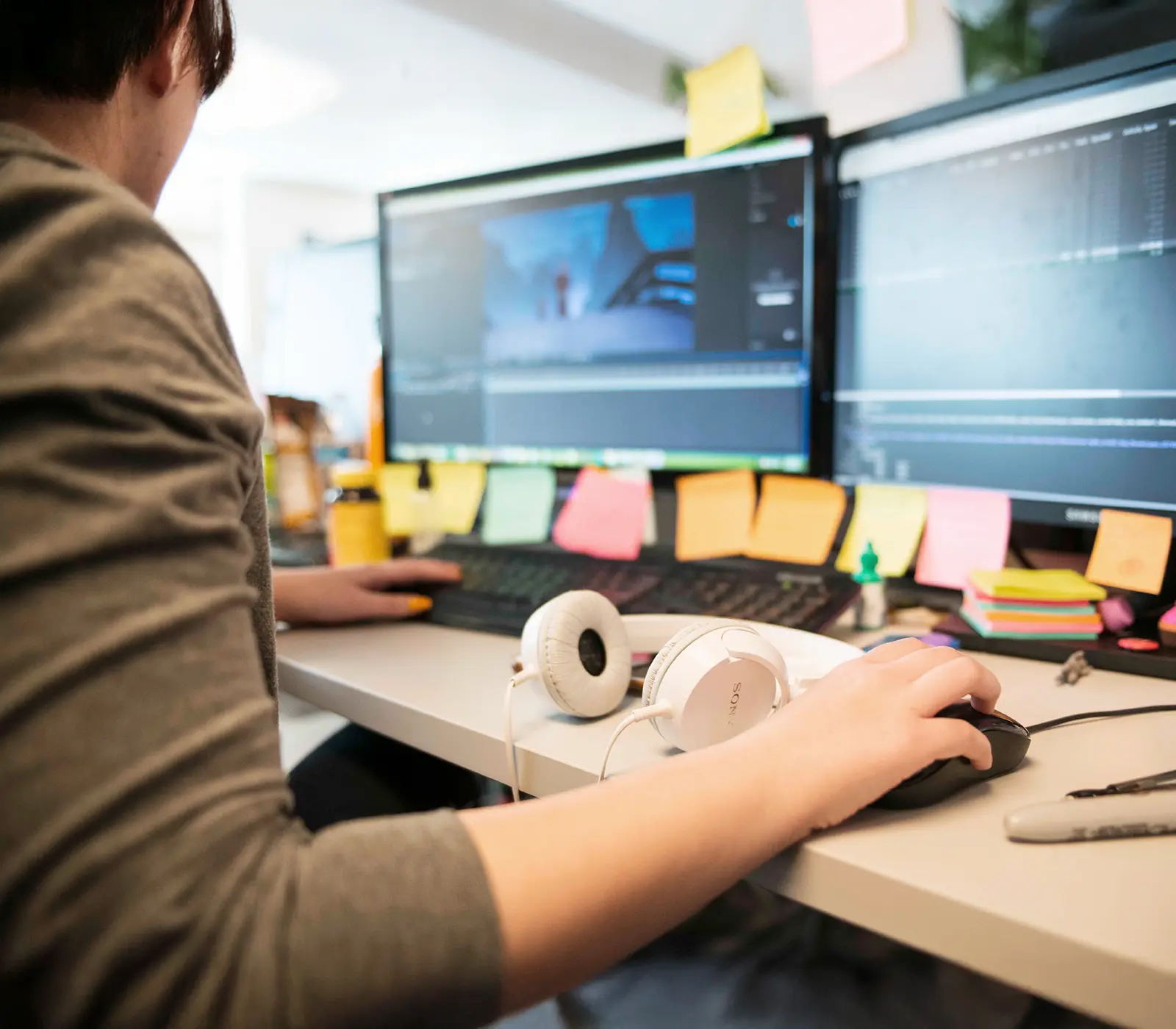 A DigiPen student works on a PC with headphones set on the desk.