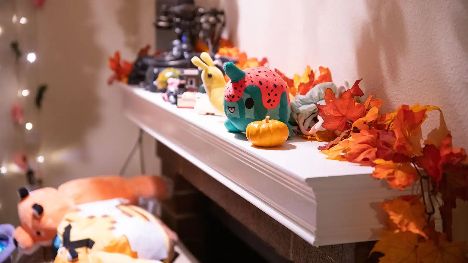 Various plushies sit on a mantle with fall decorations.