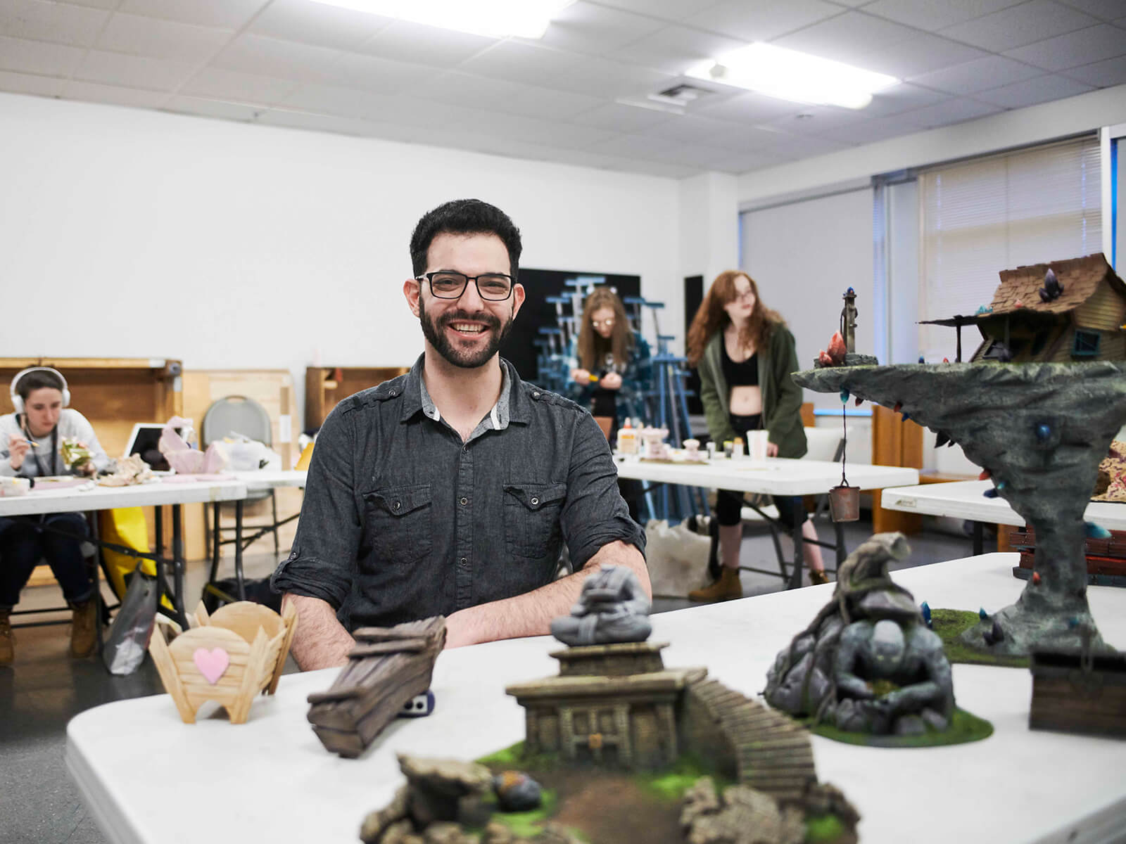 Professor Danny Samuels poses in front of student work in his miniature set design class. 