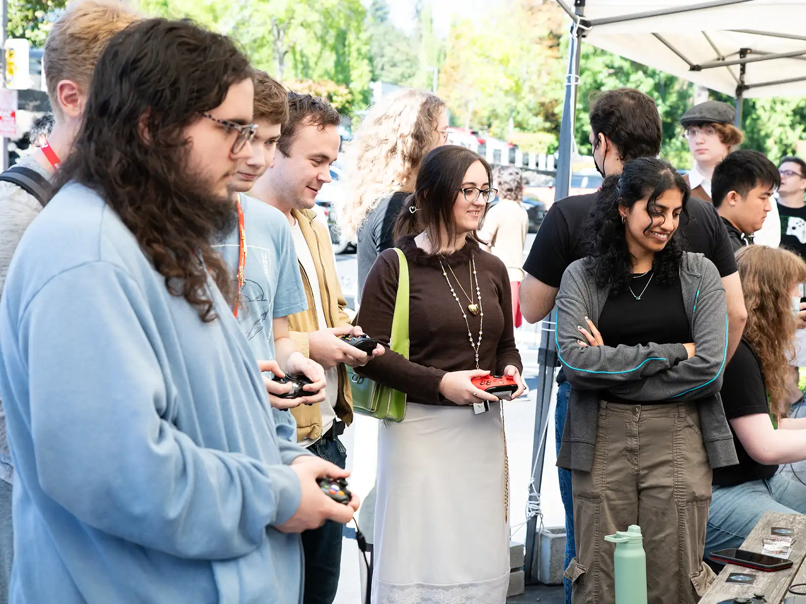 Four DigiPen students holding controllers play a game side-by-side with one onlooker standing outside of campus.