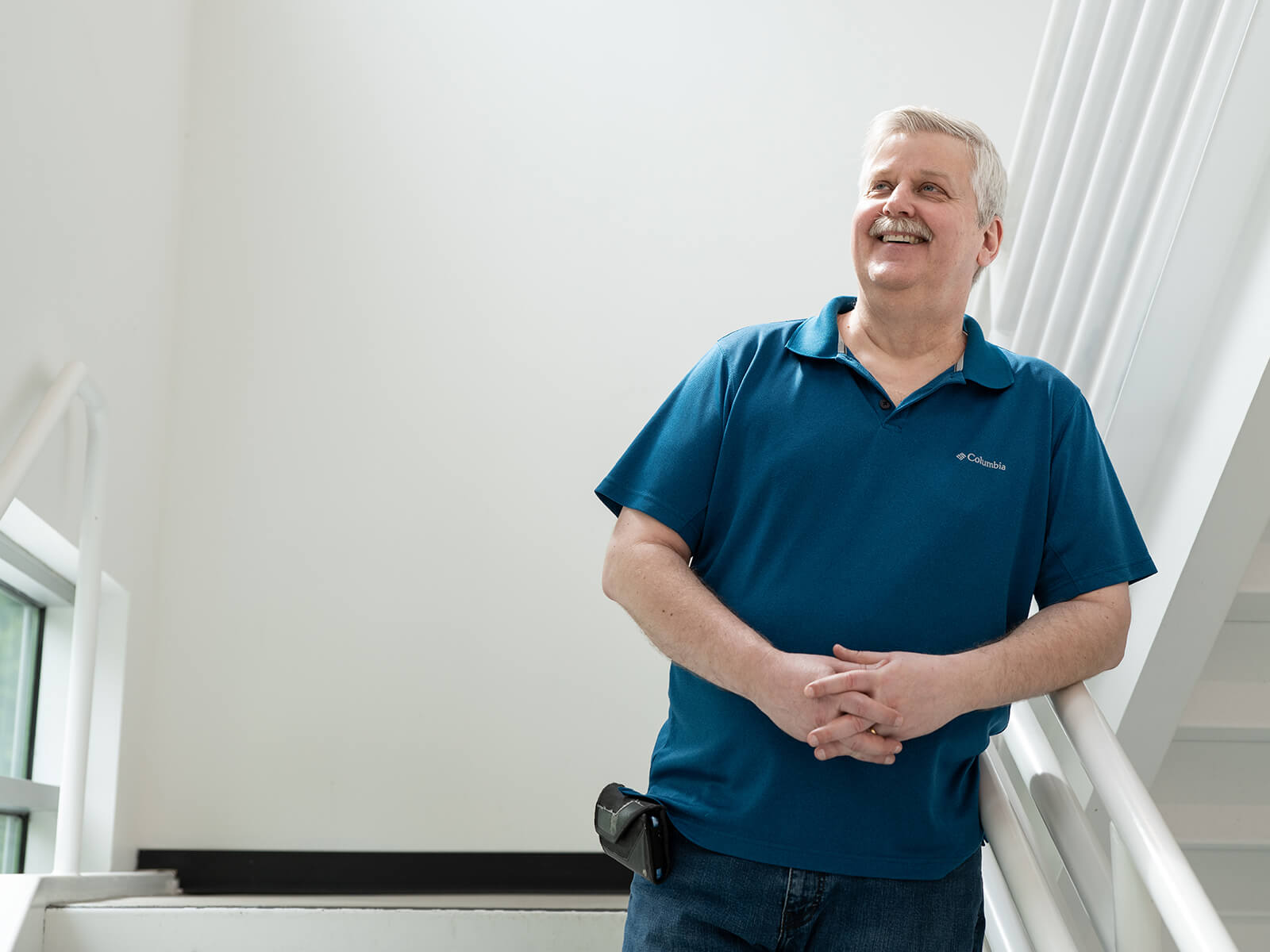 Doug Schilling smiles with his hands folded in a bright white stairwell. 