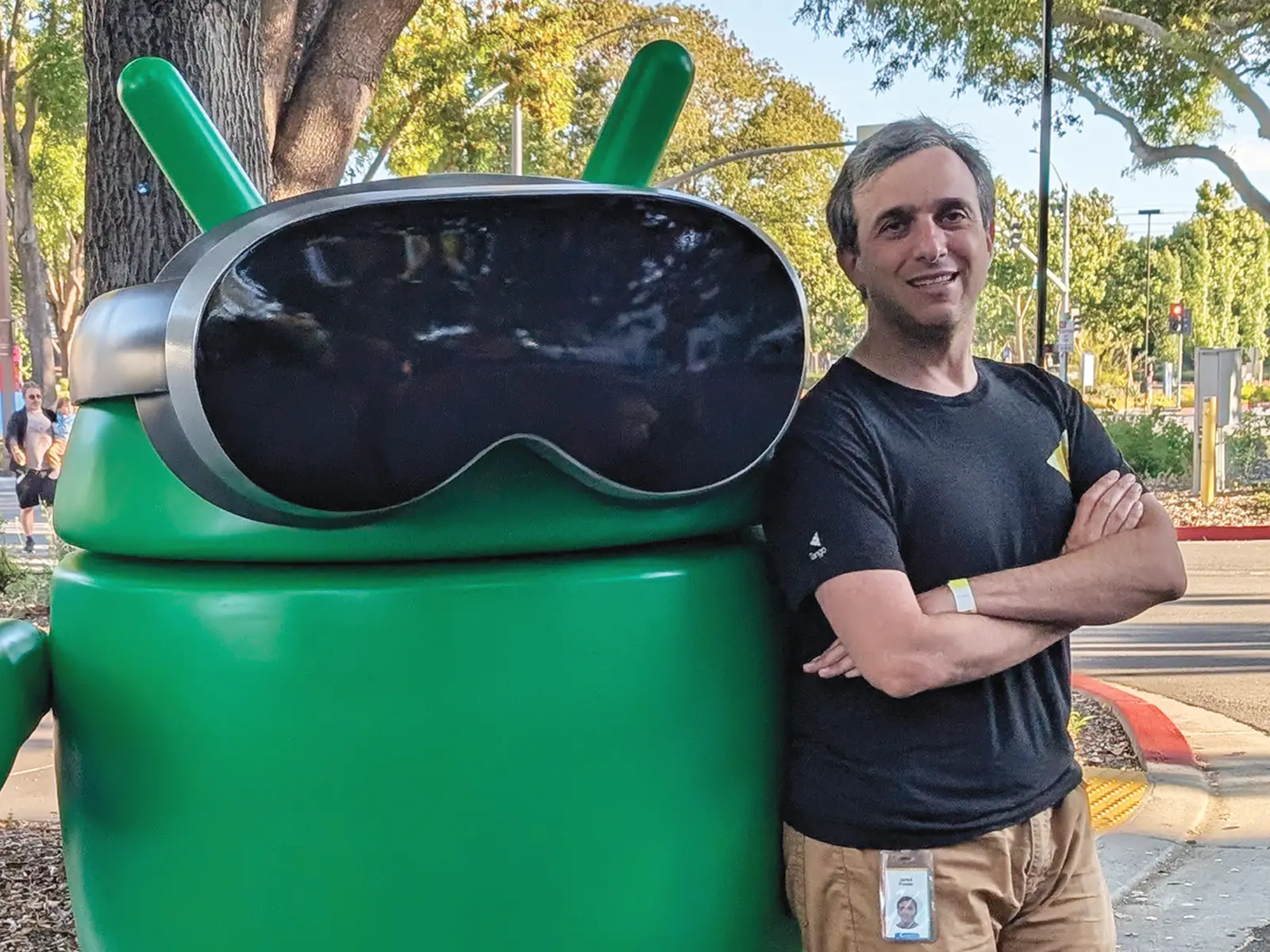 Jared Finder poses next to a statue of the Google Android mascot wearing a VR headset.