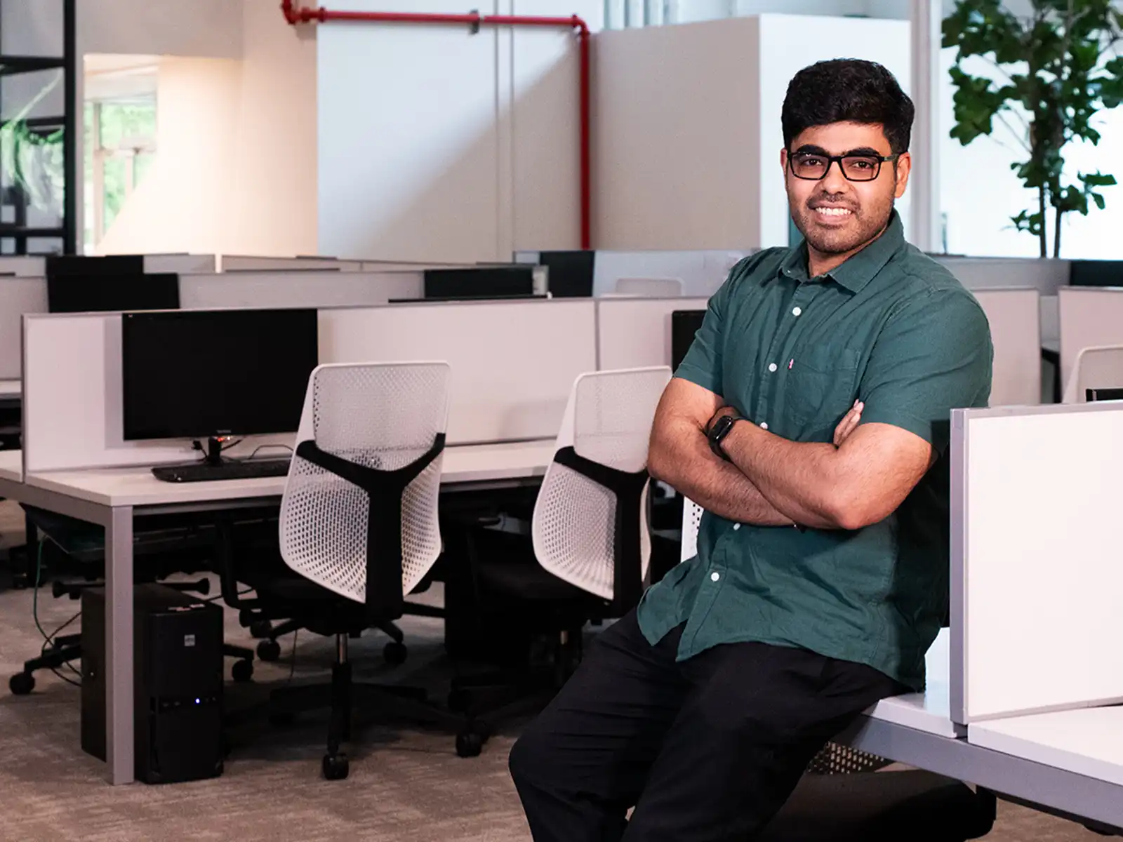 Aakash Chotrani smiles with his arms crossed leaning on a computer bay in DigiPen’s Wing building on campus.
