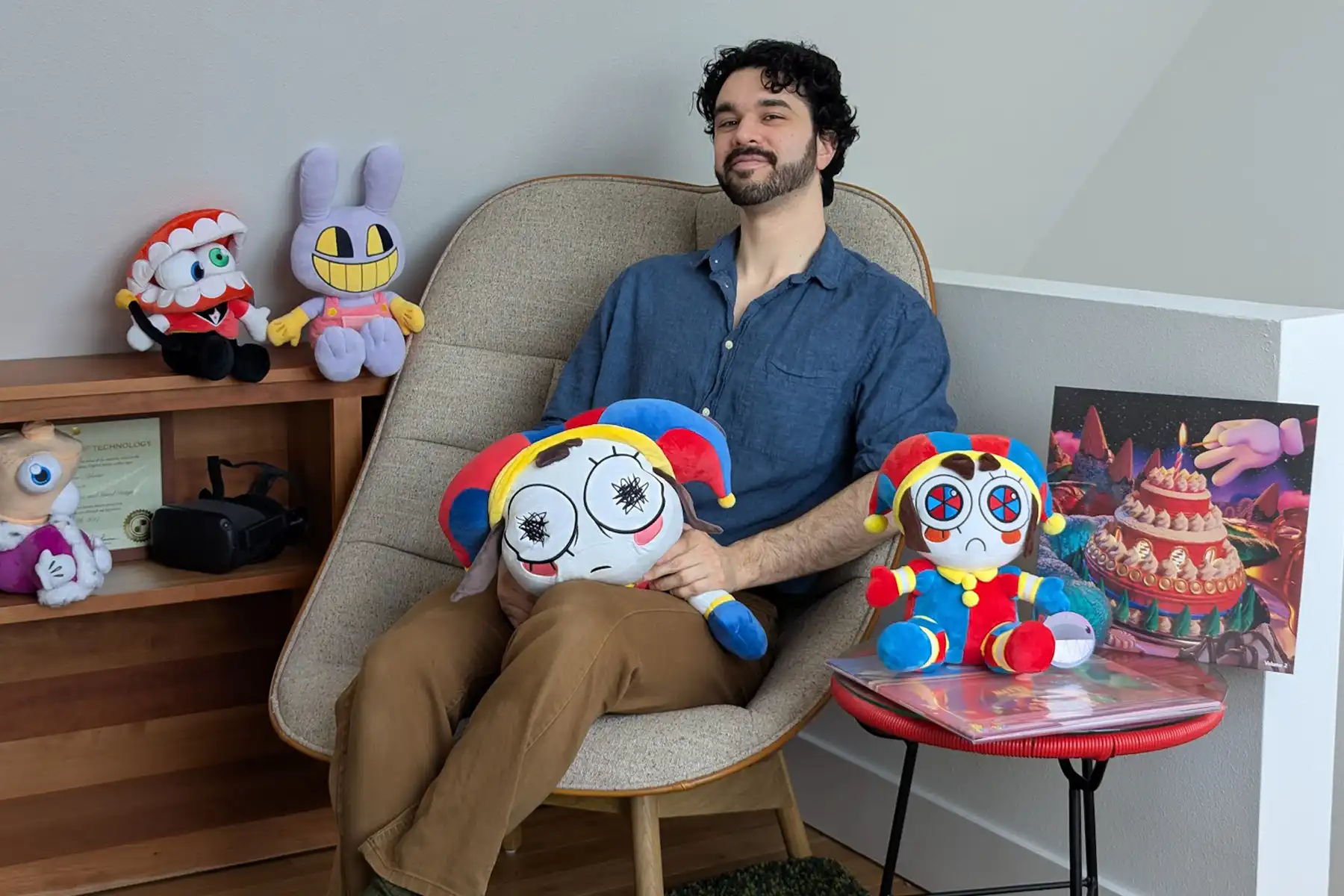 Evan Alderete poses in a chair holding a Pomni plushie surrounded by other stuffed dolls of Amazing Digital Circus characters.