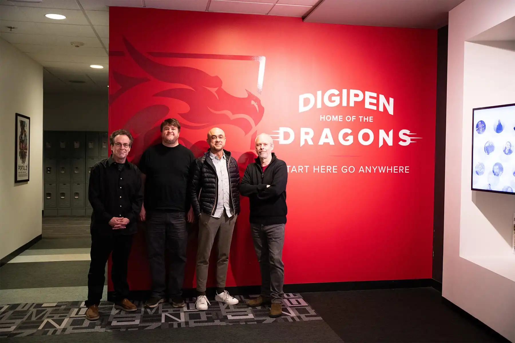 Four DigiPen music faculty pose together in front of a wall bearing the DigiPen Dragon logo.