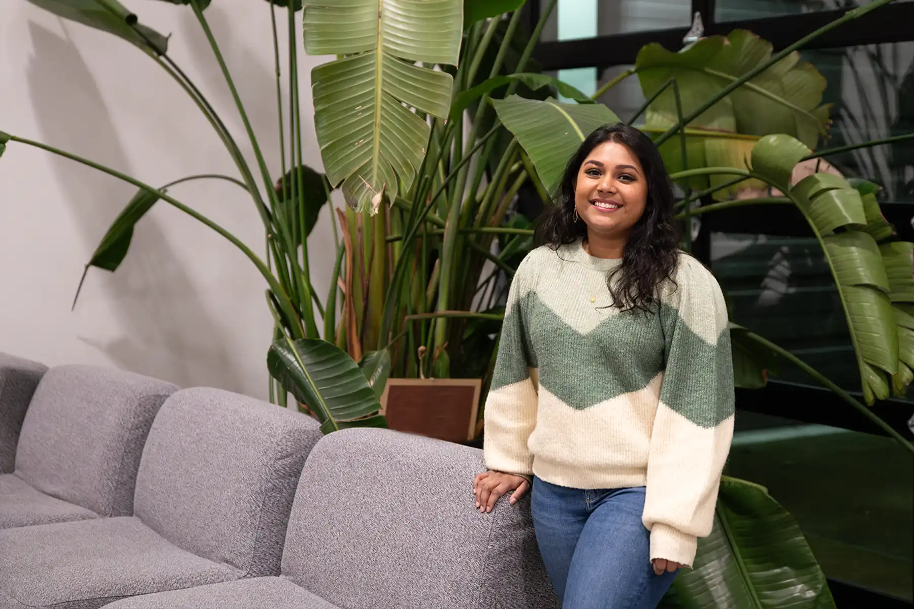 Neha Chintala smiles in front of a couch and large potted plant on DigiPen’s campus.