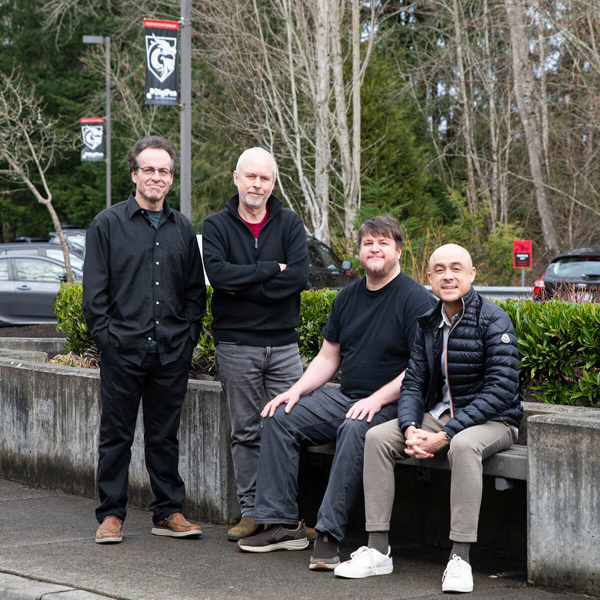 DigiPen music faculty pose by a concrete bench in the DigiPen parking lot surrounded by trees.