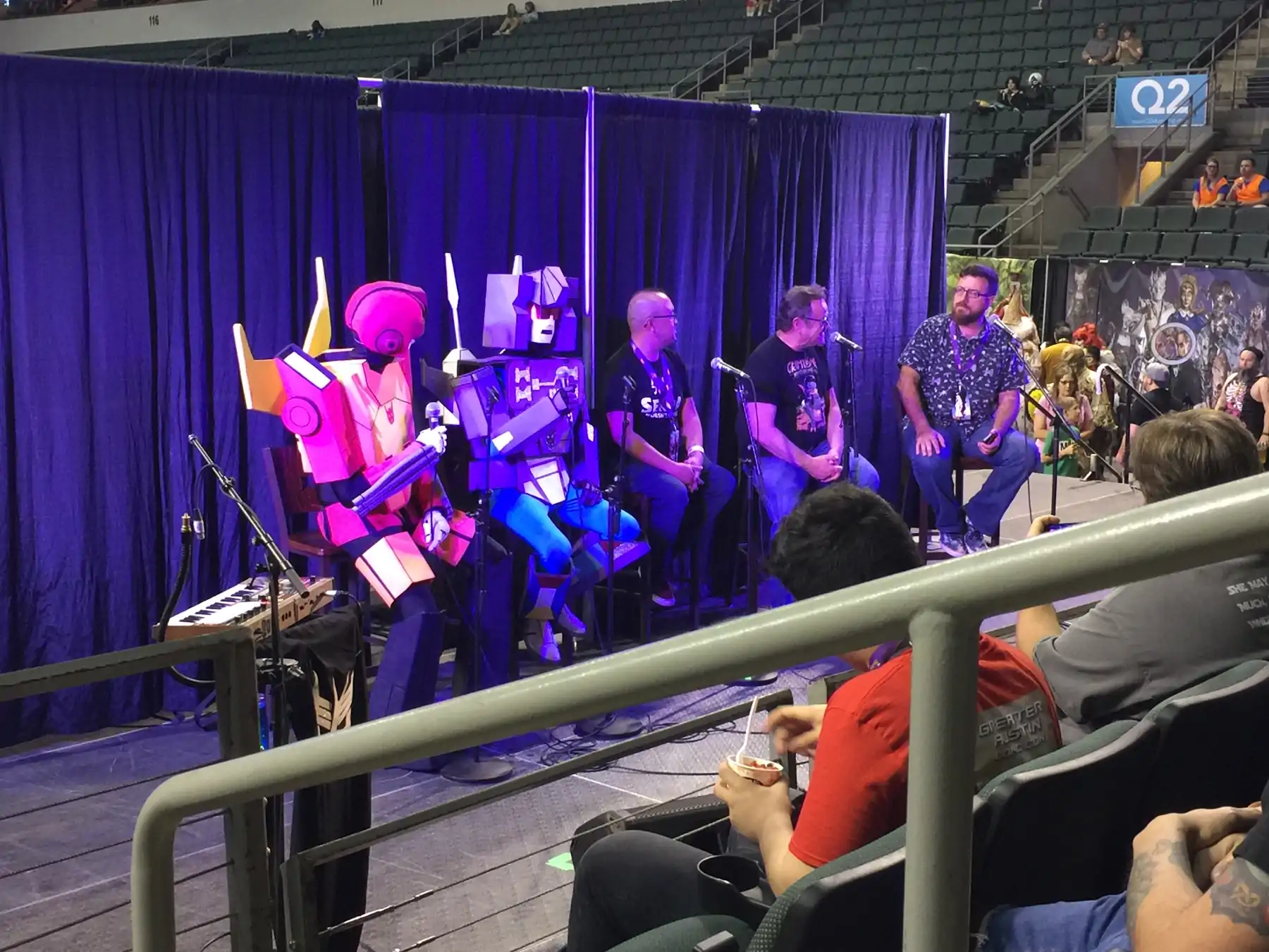 Transformers cosplayers seated next to other convention panel speakers on a stage