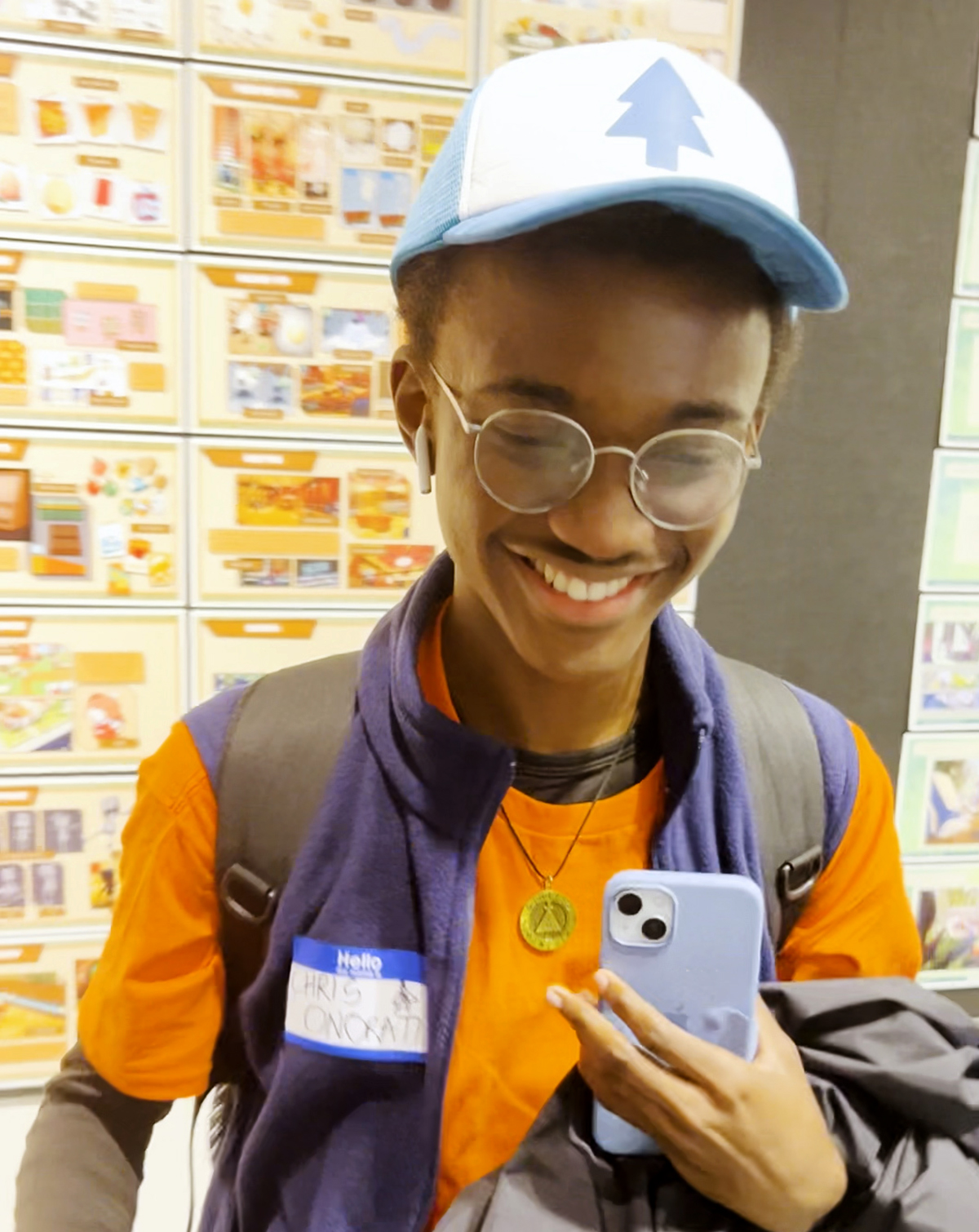 A student wears a name tag with “Chris Onorati” on it, wearing his iconic hat and vest.