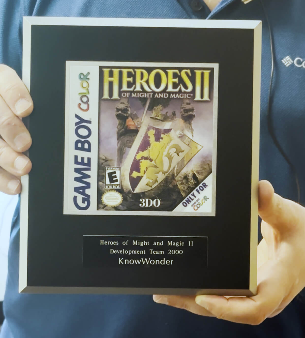 Douglas Schilling holds a plaque featuring game box art commemorating his work on Heroes of Might and Magic for the Game Boy Color.
