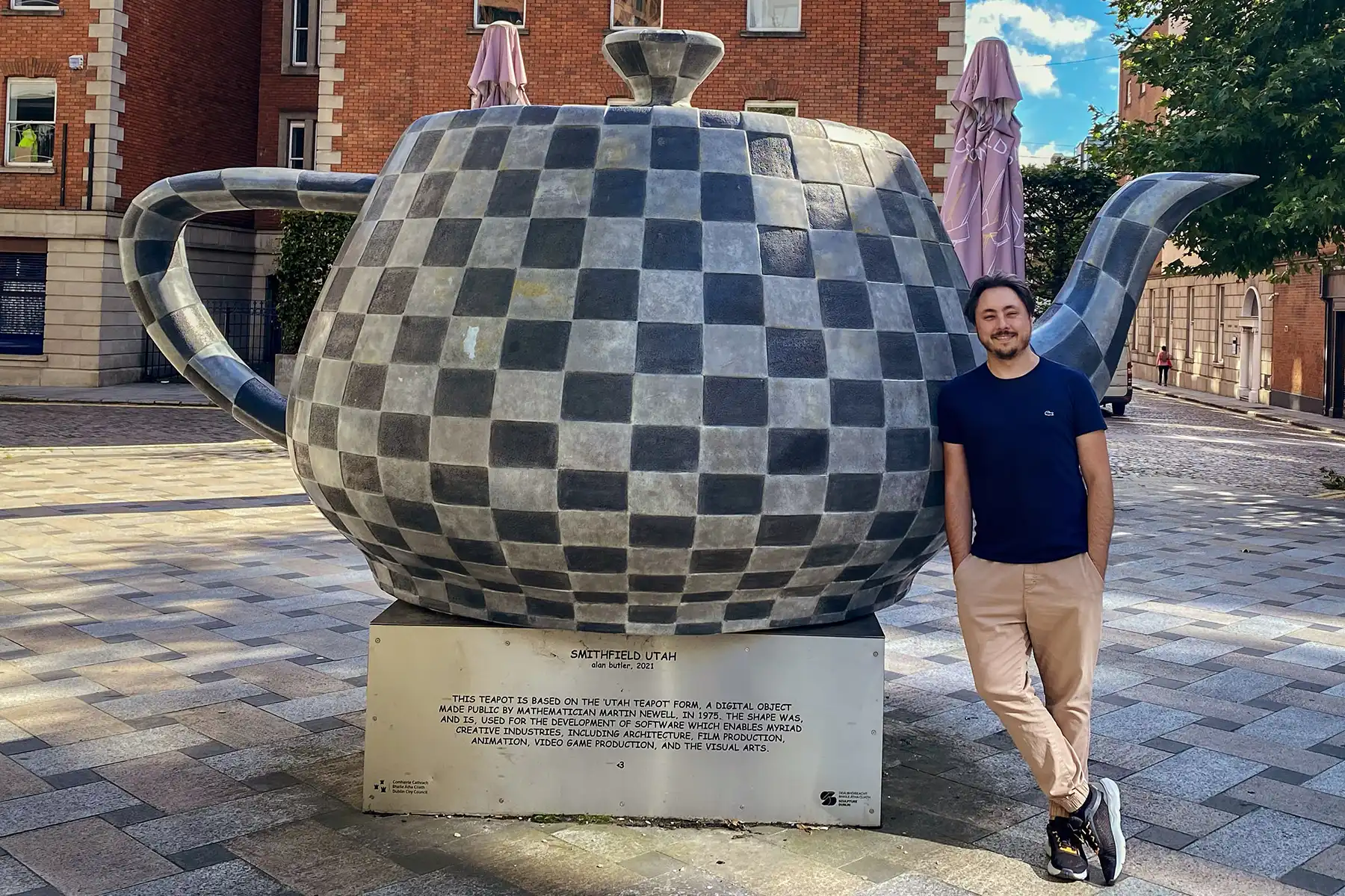 Eduardo Righi Chaves smiles and leans against a large, checkered sculpture of a teapot.