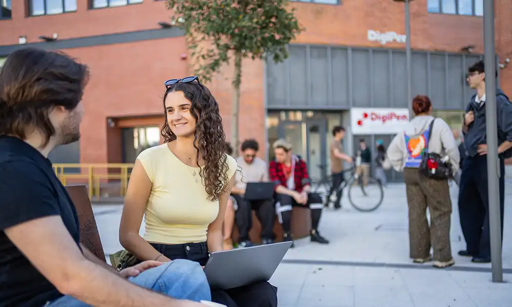Two students sit outside entrance of DigiPen Bilbao.